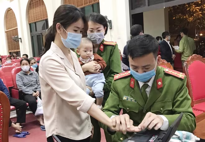 Trung tá Nguyễn Thị Hiền, Phó Đội trưởng Đội Cảnh sát QLHC về TTXH - CAH Hoài Đức bế con cho công dân để họ lăn tay, chụp ảnh làm căn cước công dân mới