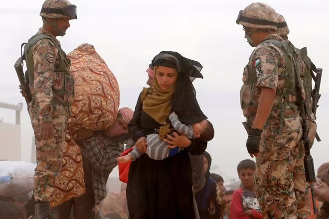 Một phụ nữ Syria bế con qua biên giới đến Jordan, nơi cùng với Thổ Nhĩ Kỳ, Lebanon, Iraq và Ai Cập tiếp nhận 5,6 triệu người tị nạn nước này